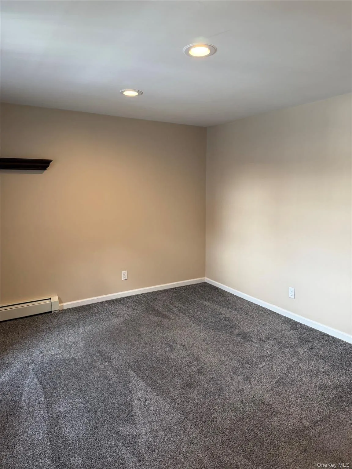 Empty room featuring recessed lighting, a baseboard radiator, and dark carpet Empty room featuring recessed lighting, a baseboard radiator, and dark carpet