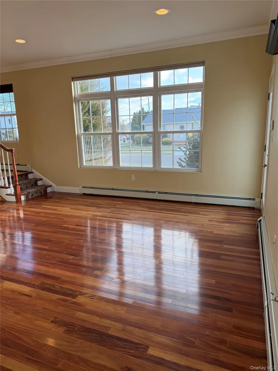 Unfurnished living room featuring crown molding, stairs, baseboard heating, dark wood-style flooring, and a baseboard heating unit Unfurnished living room featuring crown molding, stairs, baseboard heating, dark wood-style flooring, and a baseboard heating unit