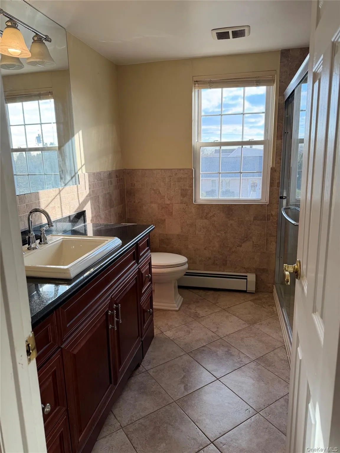 Full bathroom featuring vanity, a shower stall, tile walls, baseboard heating, and plenty of natural light Full bathroom featuring vanity, a shower stall, tile walls, baseboard heating, and plenty of natural light