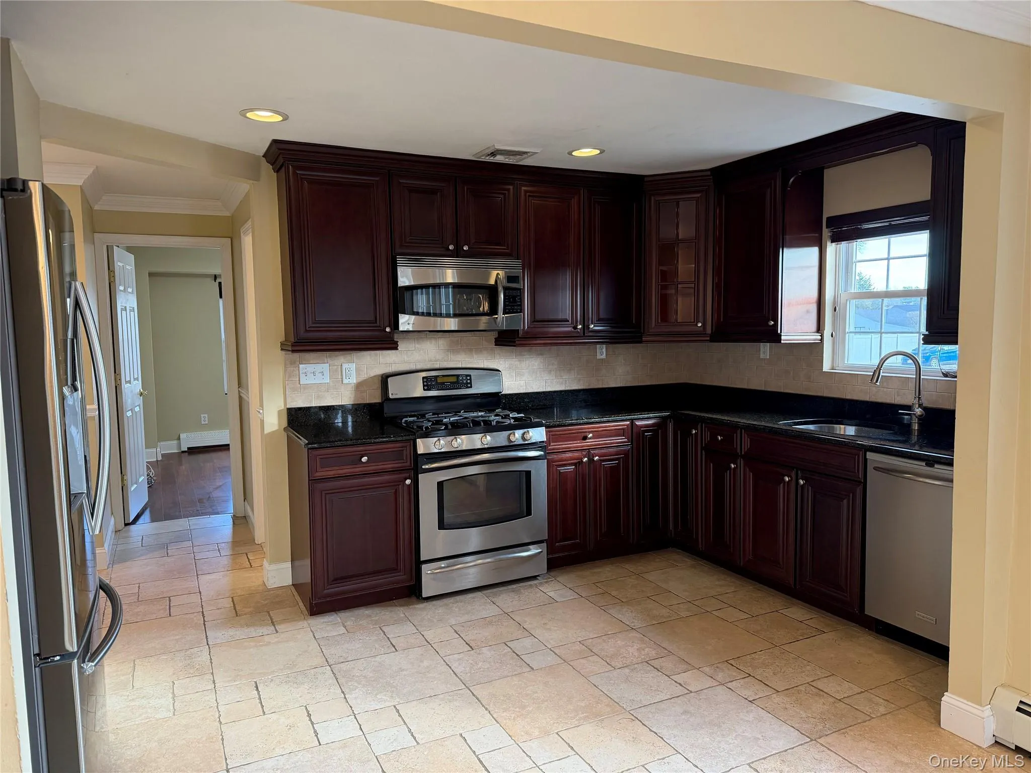 Kitchen with stainless steel appliances, dark brown cabinets, ornamental molding, dark stone counters, and recessed lighting Kitchen with stainless steel appliances, dark brown cabinets, ornamental molding, dark stone counters, and recessed lighting