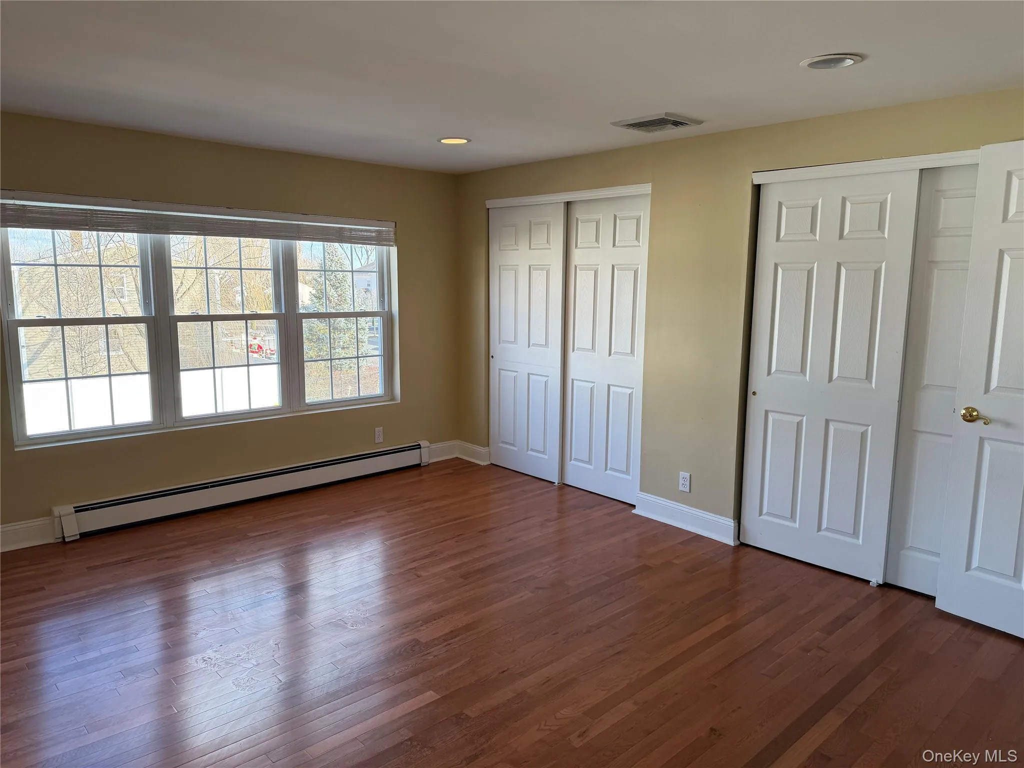 Unfurnished bedroom featuring two closets, a baseboard radiator, dark wood-style floors, and recessed lighting Unfurnished bedroom featuring two closets, a baseboard radiator, dark wood-style floors, and recessed lighting
