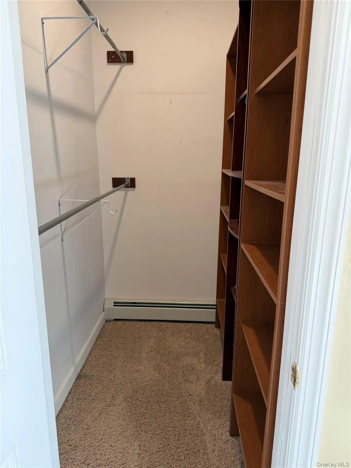 Walk in closet featuring a baseboard radiator and light colored carpet Walk in closet featuring a baseboard radiator and light colored carpet