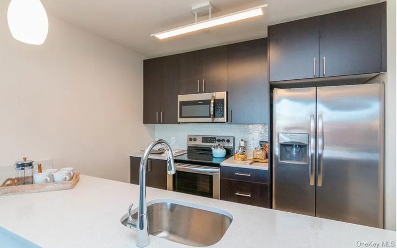 Kitchen with stainless steel appliances, decorative backsplash, light stone counters, modern cabinets, and dark brown cabinets Kitchen with stainless steel appliances, decorative backsplash, light stone counters, modern cabinets, and dark brown cabinets