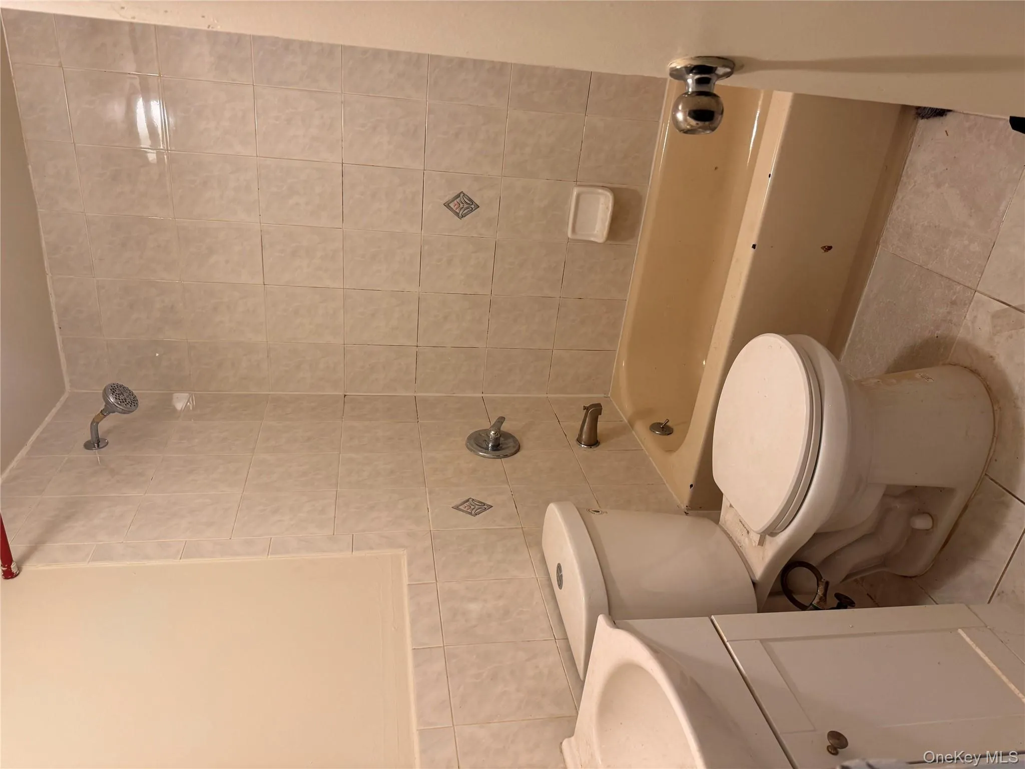 Full bathroom with vanity, tile walls, shower combination, and light tile patterned floors Full bathroom with vanity, tile walls, shower combination, and light tile patterned floors
