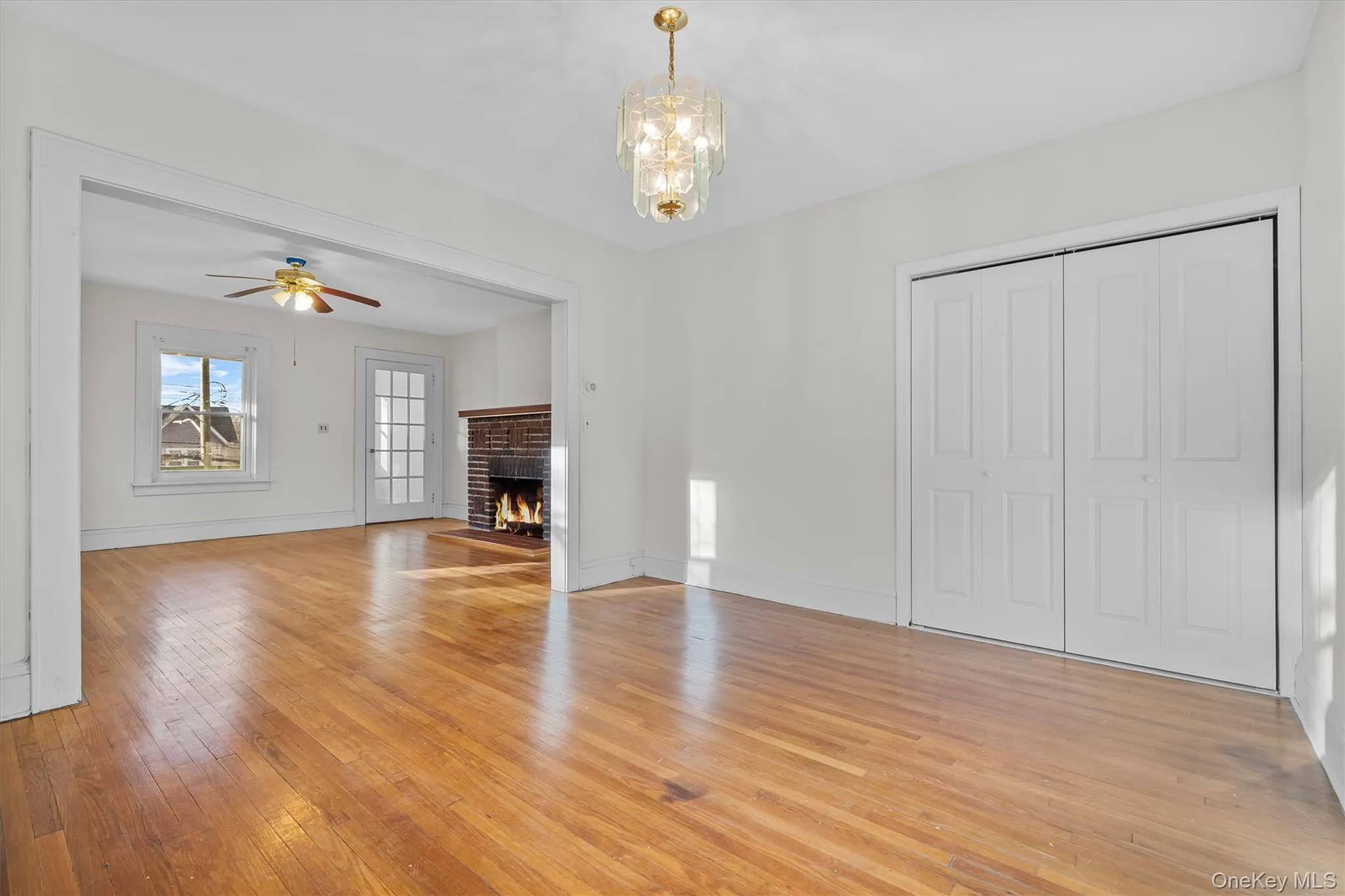 Unfurnished living room with light wood-type flooring, a brick fireplace, and a chandelier Unfurnished living room with light wood-type flooring, a brick fireplace, and a chandelier