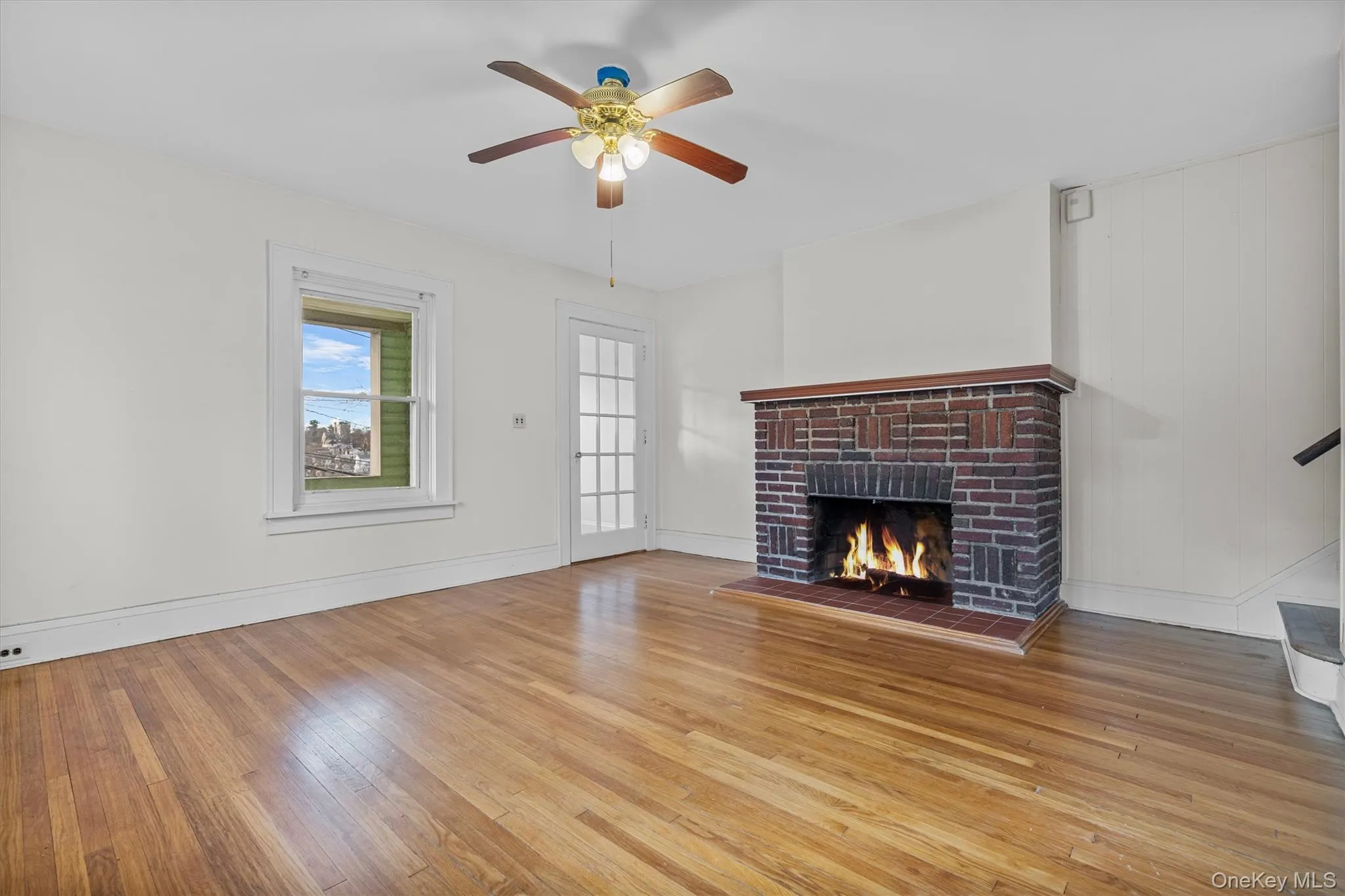 Unfurnished living room featuring a brick fireplace, light wood-type flooring, and a ceiling fan Unfurnished living room featuring a brick fireplace, light wood-type flooring, and a ceiling fan