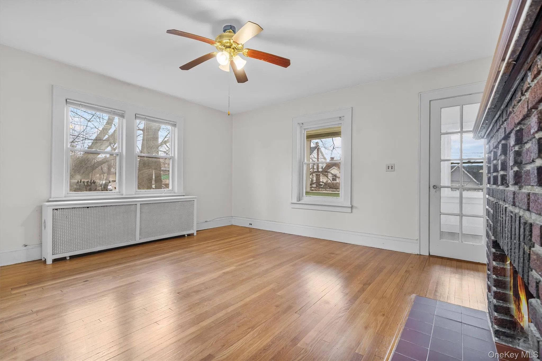 Spare room with radiator heating unit, light wood-style flooring, a fireplace, and ceiling fan Spare room with radiator heating unit, light wood-style flooring, a fireplace, and ceiling fan