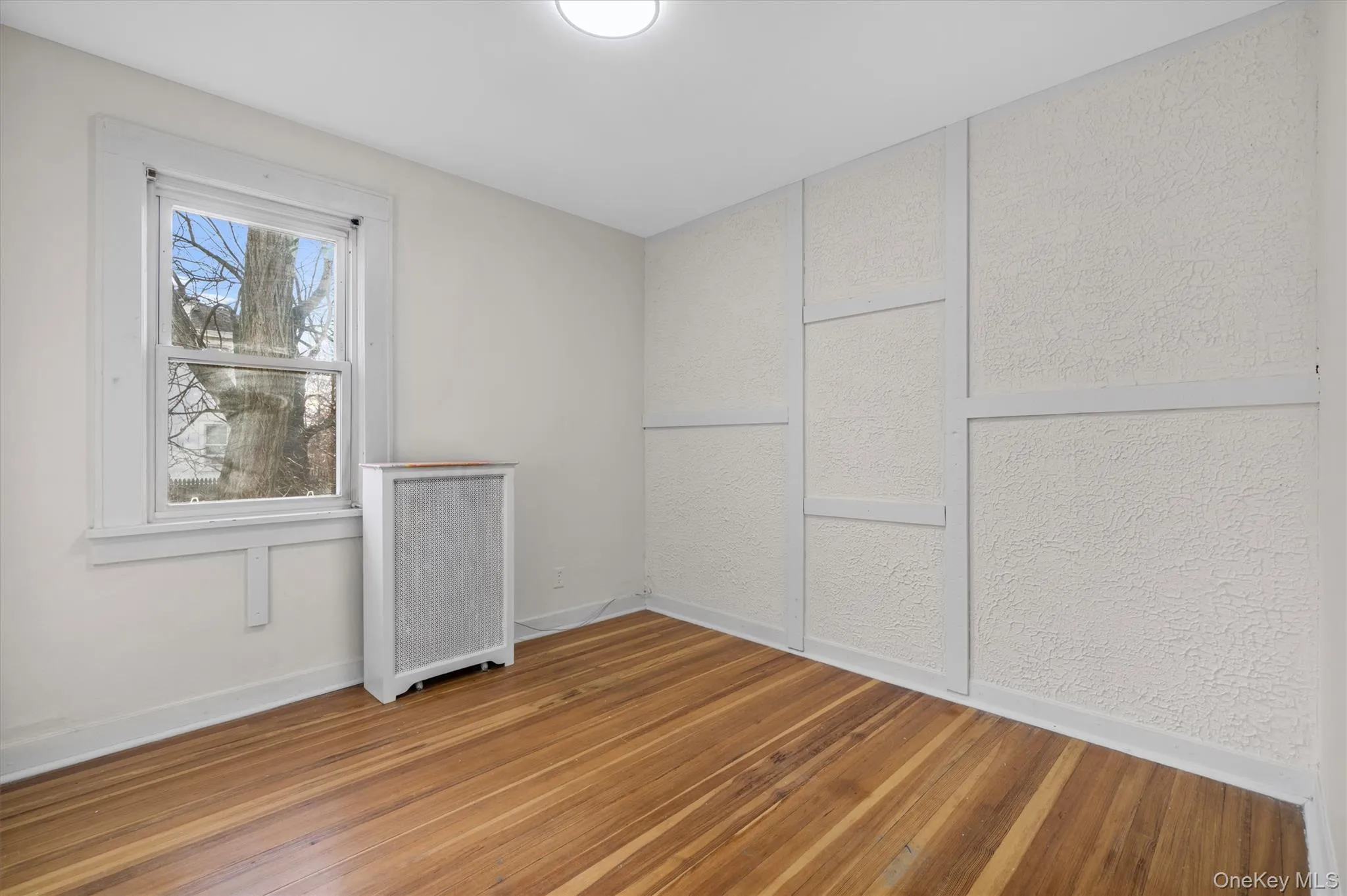Spare room featuring hardwood / wood-style flooring, radiator heating unit, and a textured wall Spare room featuring hardwood / wood-style flooring, radiator heating unit, and a textured wall