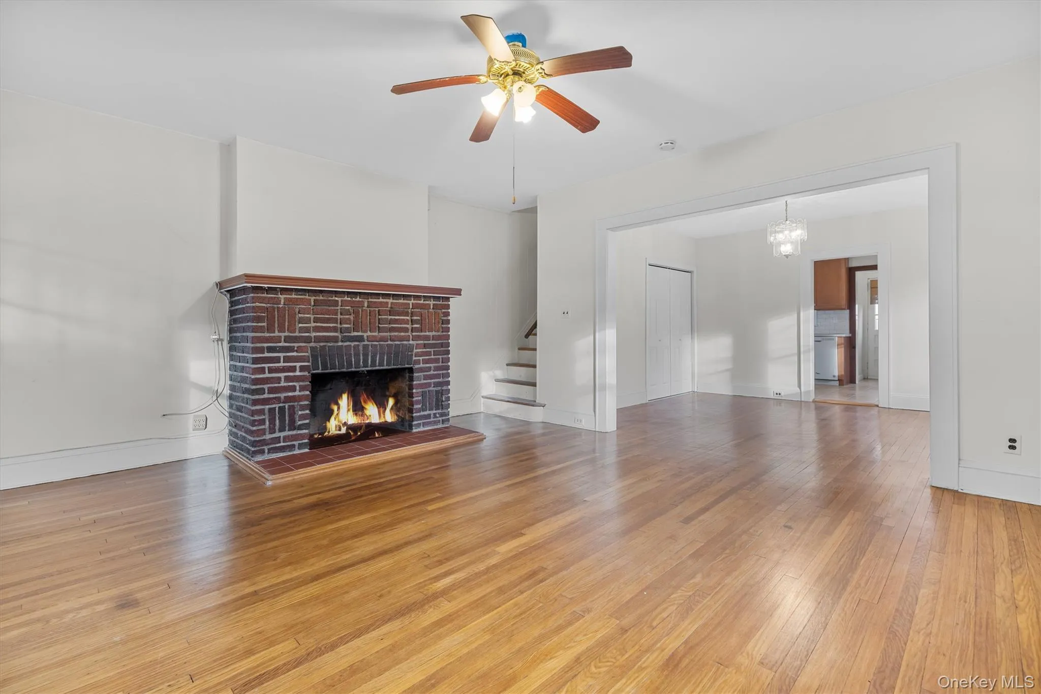 Unfurnished living room with light wood-type flooring, a fireplace, stairs, ceiling fan, and a chandelier Unfurnished living room with light wood-type flooring, a fireplace, stairs, ceiling fan, and a chandelier