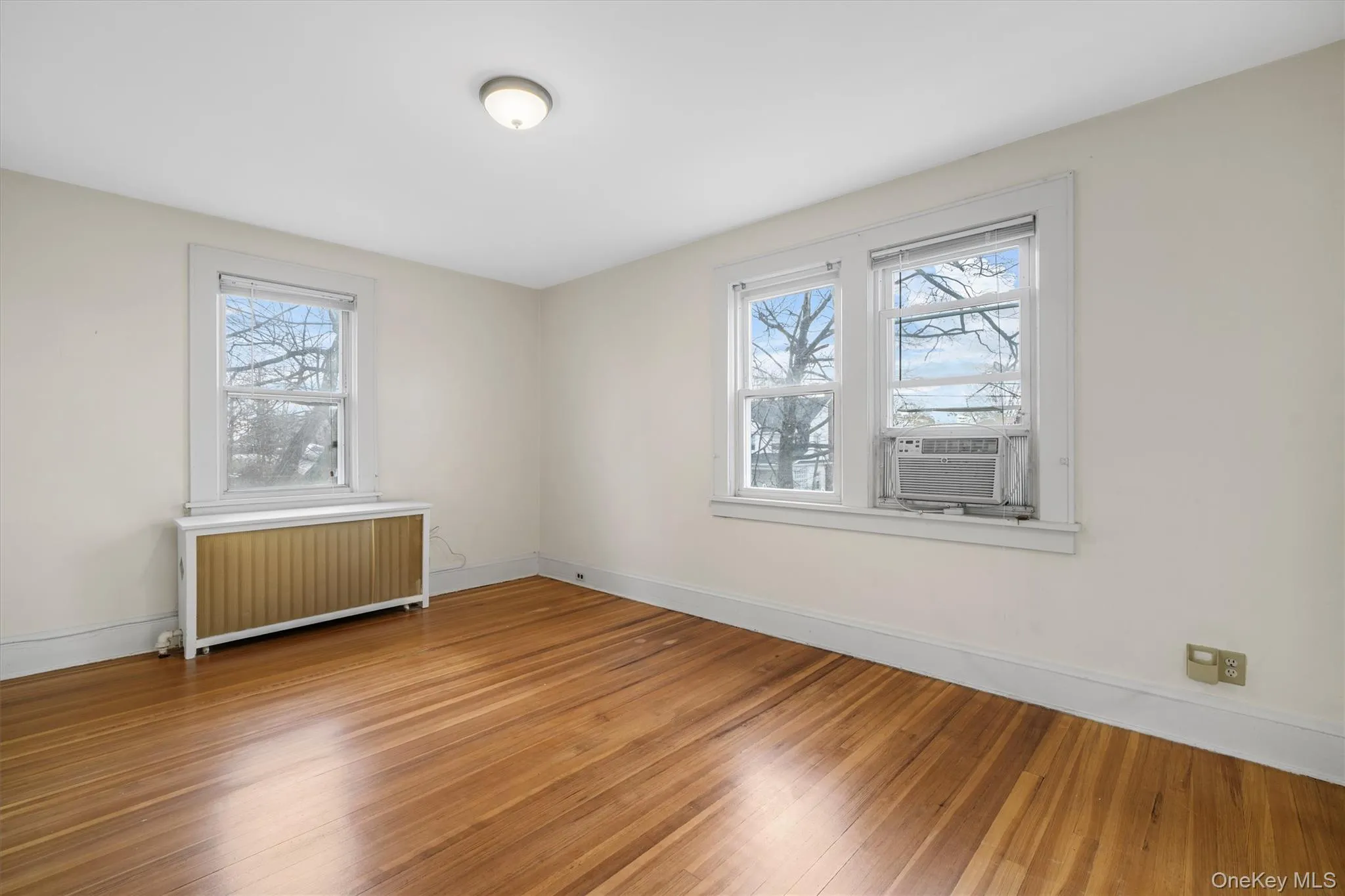 Empty room with radiator, hardwood / wood-style flooring, and cooling unit Empty room with radiator, hardwood / wood-style flooring, and cooling unit