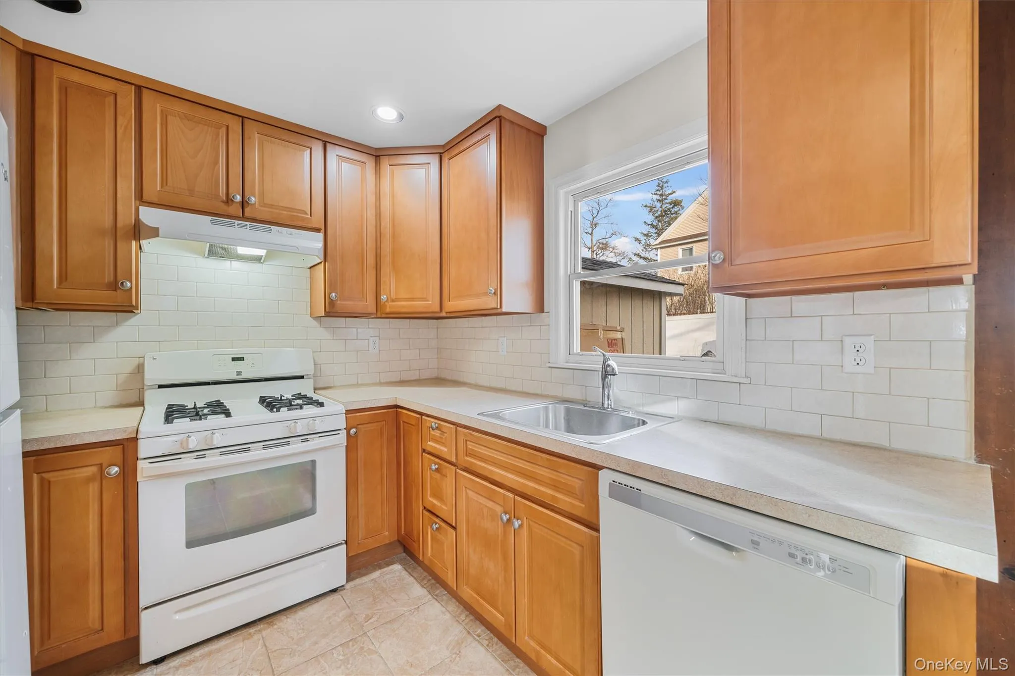 Kitchen featuring white appliances, light countertops, under cabinet range hood, brown cabinets, and recessed lighting Kitchen featuring white appliances, light countertops, under cabinet range hood, brown cabinets, and recessed lighting