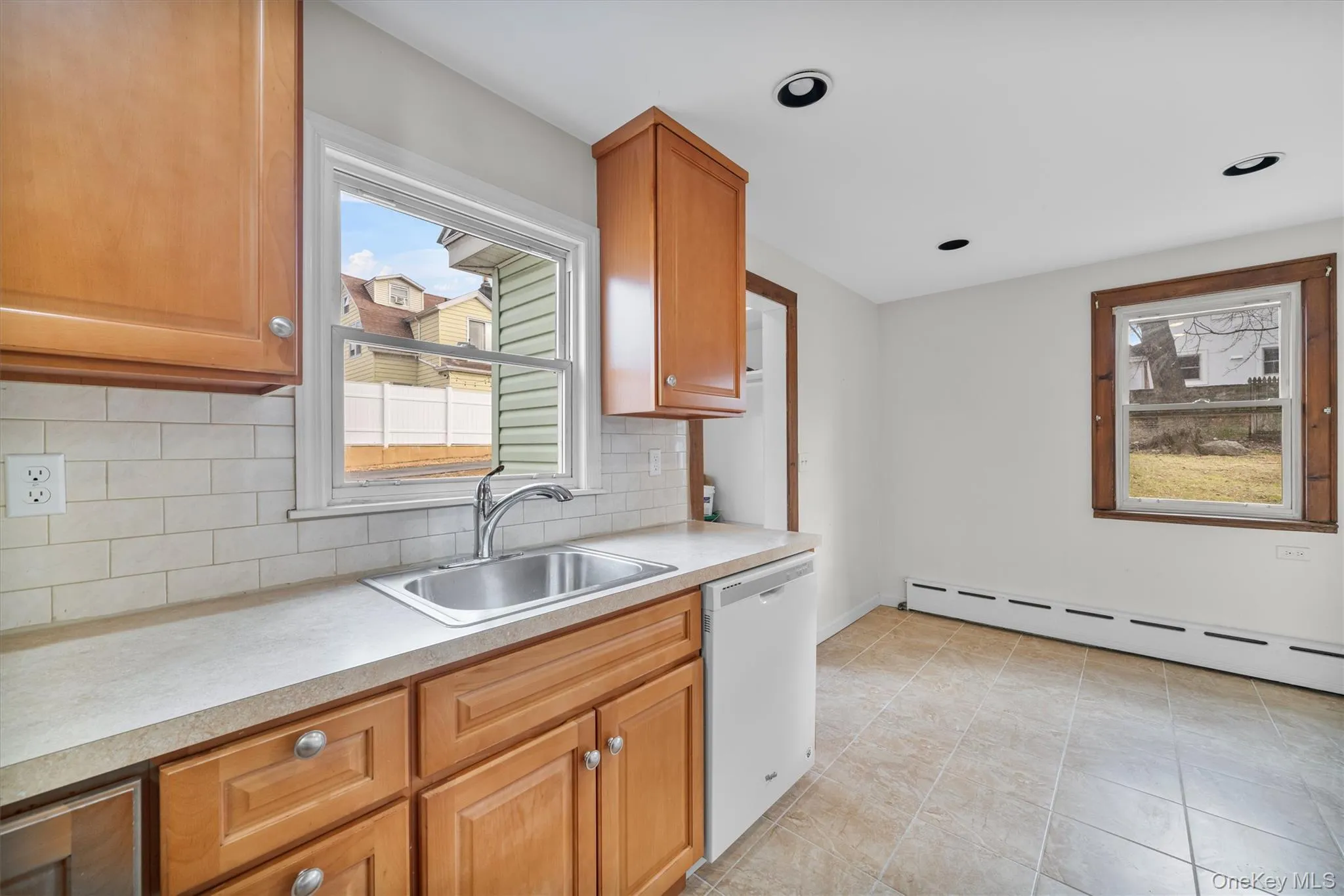 Kitchen featuring dishwasher, baseboard heating, brown cabinets, decorative backsplash, and light countertops Kitchen featuring dishwasher, baseboard heating, brown cabinets, decorative backsplash, and light countertops