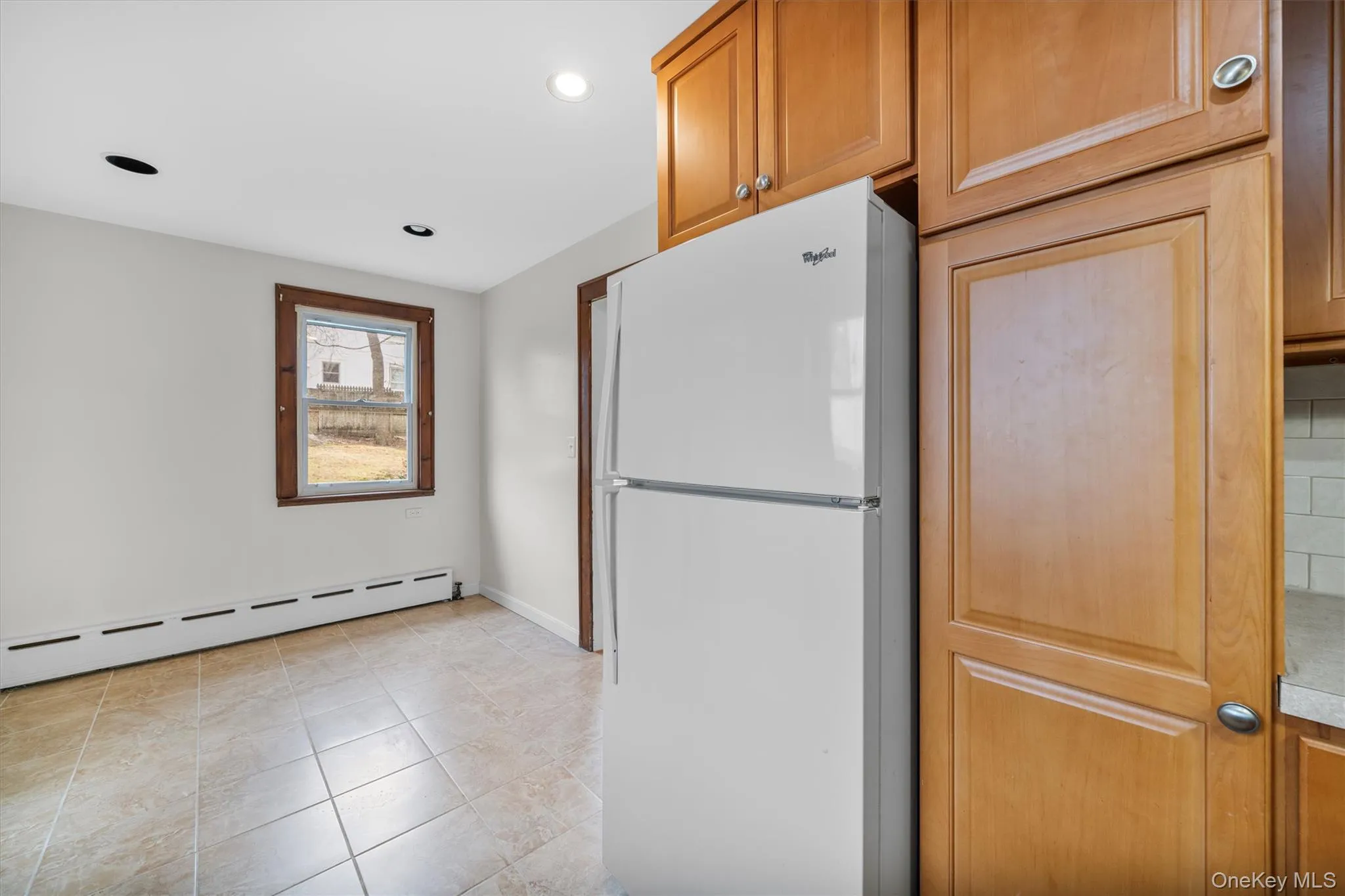 Kitchen featuring freestanding refrigerator, brown cabinets, a baseboard radiator, light tile patterned floors, and recessed lighting Kitchen featuring freestanding refrigerator, brown cabinets, a baseboard radiator, light tile patterned floors, and recessed lighting