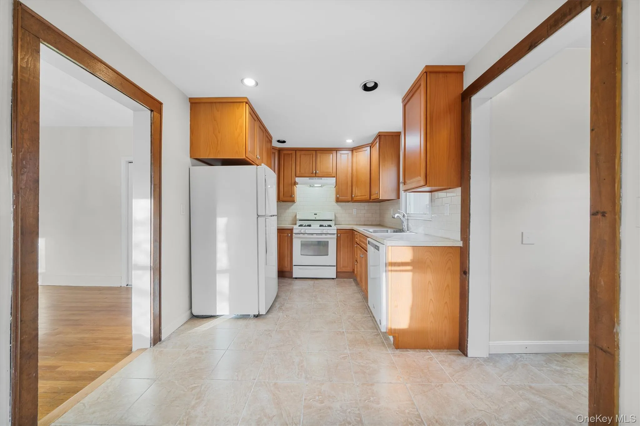 Kitchen with white appliances, light countertops, brown cabinetry, tasteful backsplash, and light tile patterned floors Kitchen with white appliances, light countertops, brown cabinetry, tasteful backsplash, and light tile patterned floors