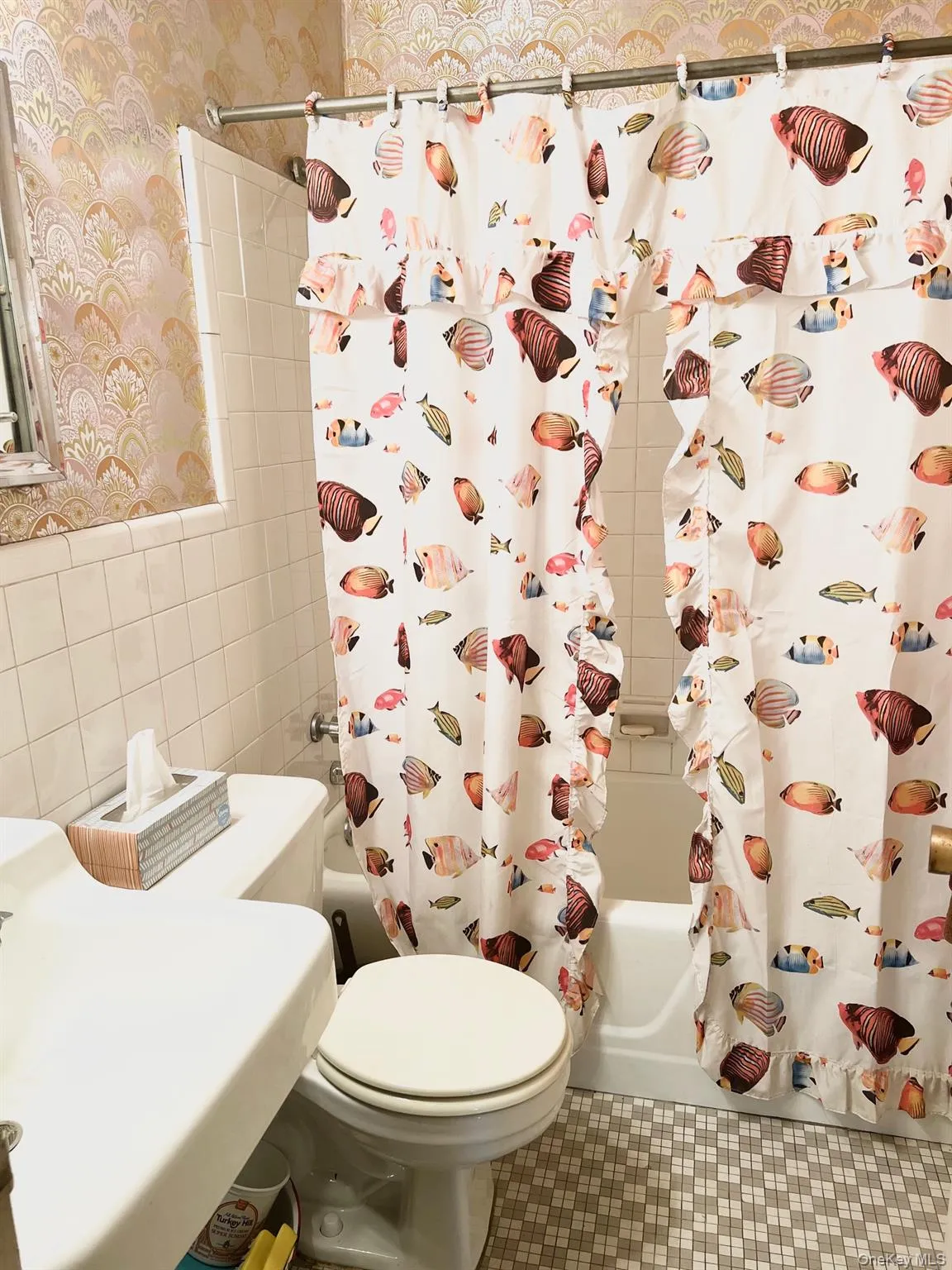 Full bathroom with shower / bath combo with shower curtain, wallpapered walls, tile walls, tile patterned floors, and wainscoting Full bathroom with shower / bath combo with shower curtain, wallpapered walls, tile walls, tile patterned floors, and wainscoting