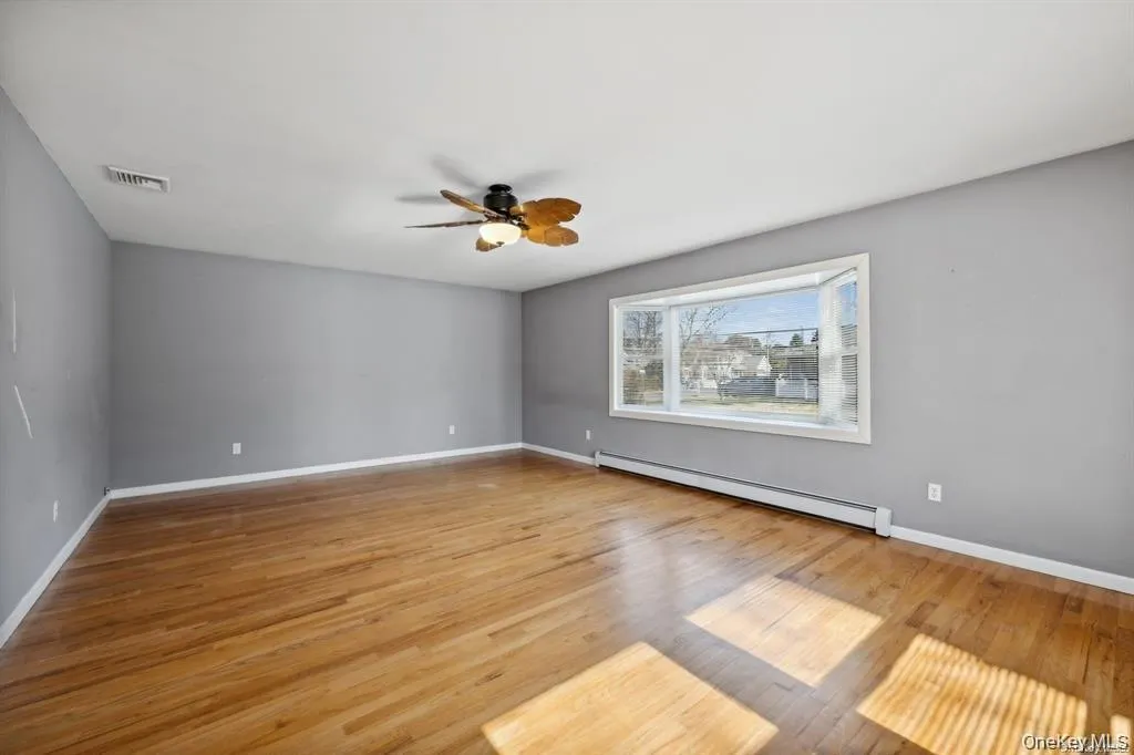 Empty room featuring a baseboard heating unit, light wood finished floors, and ceiling fan Empty room featuring a baseboard heating unit, light wood finished floors, and ceiling fan