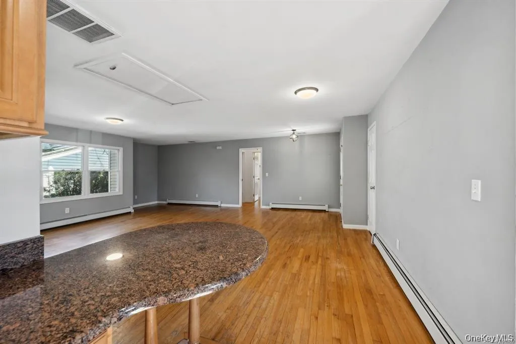 Unfurnished living room with a baseboard radiator, light wood finished floors, and attic access Unfurnished living room with a baseboard radiator, light wood finished floors, and attic access