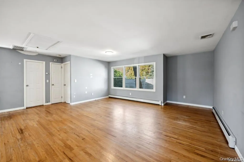 Empty room featuring baseboard heating, light wood-style floors, and attic access Empty room featuring baseboard heating, light wood-style floors, and attic access