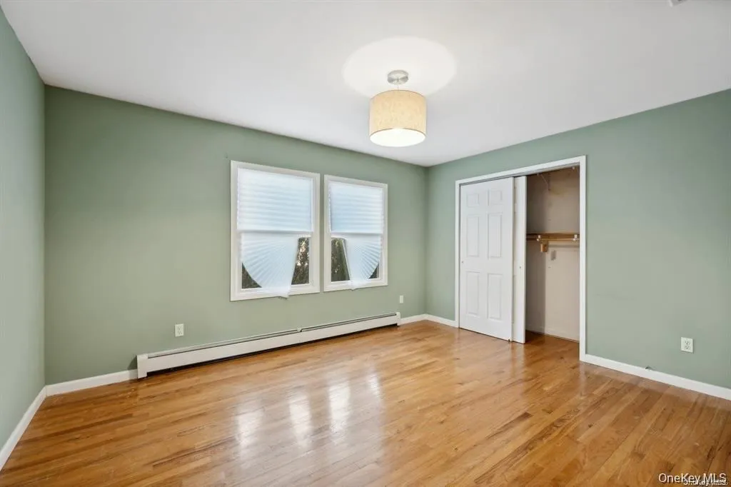 Unfurnished bedroom with baseboard heating, light wood finished floors, and a closet Unfurnished bedroom with baseboard heating, light wood finished floors, and a closet