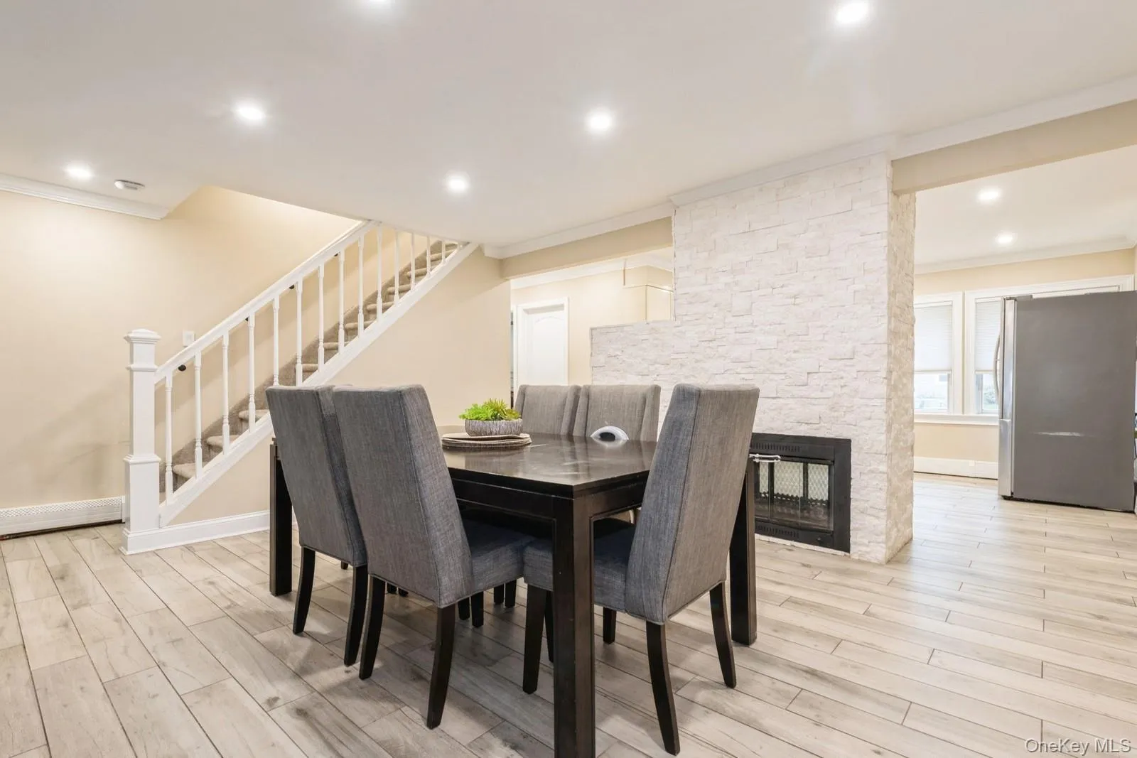 Dining space featuring crown molding, light wood-style flooring, stairway, recessed lighting, and a stone fireplace Dining space featuring crown molding, light wood-style flooring, stairway, recessed lighting, and a stone fireplace