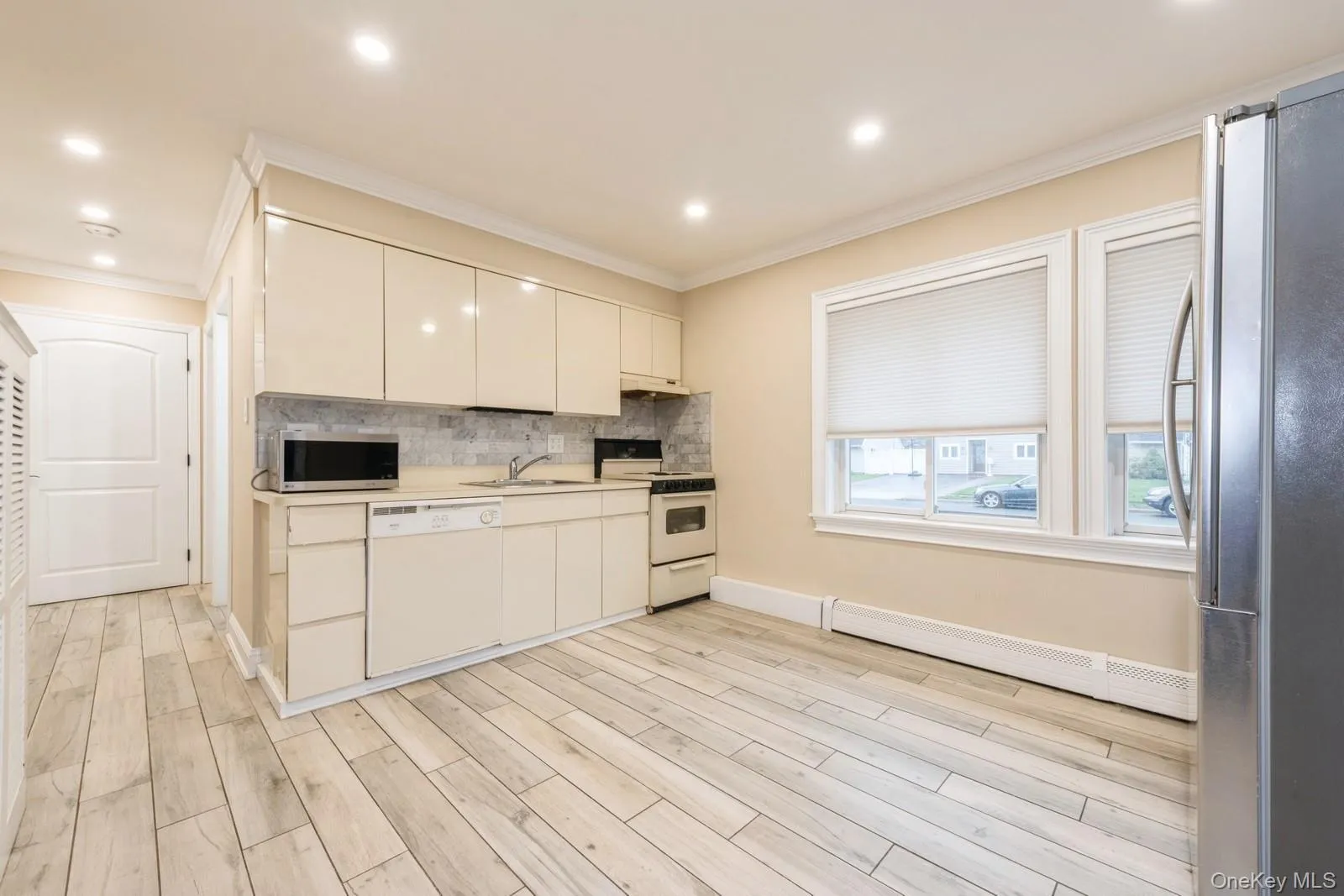 Kitchen featuring stainless steel appliances, light countertops, a baseboard radiator, crown molding, and wood tiled floors Kitchen featuring stainless steel appliances, light countertops, a baseboard radiator, crown molding, and wood tiled floors