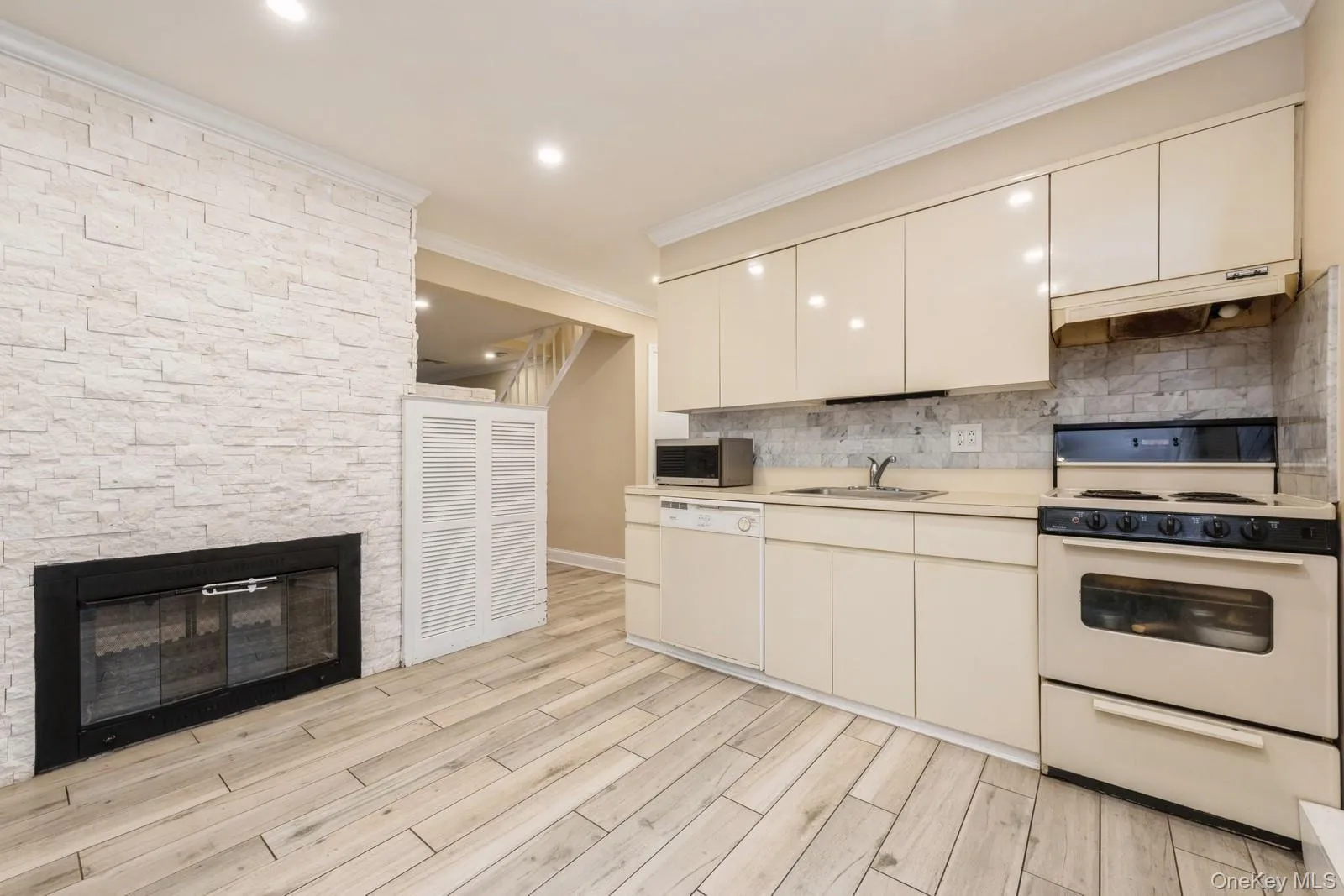 Kitchen with white appliances, light countertops, a stone fireplace, ornamental molding, and under cabinet range hood Kitchen with white appliances, light countertops, a stone fireplace, ornamental molding, and under cabinet range hood