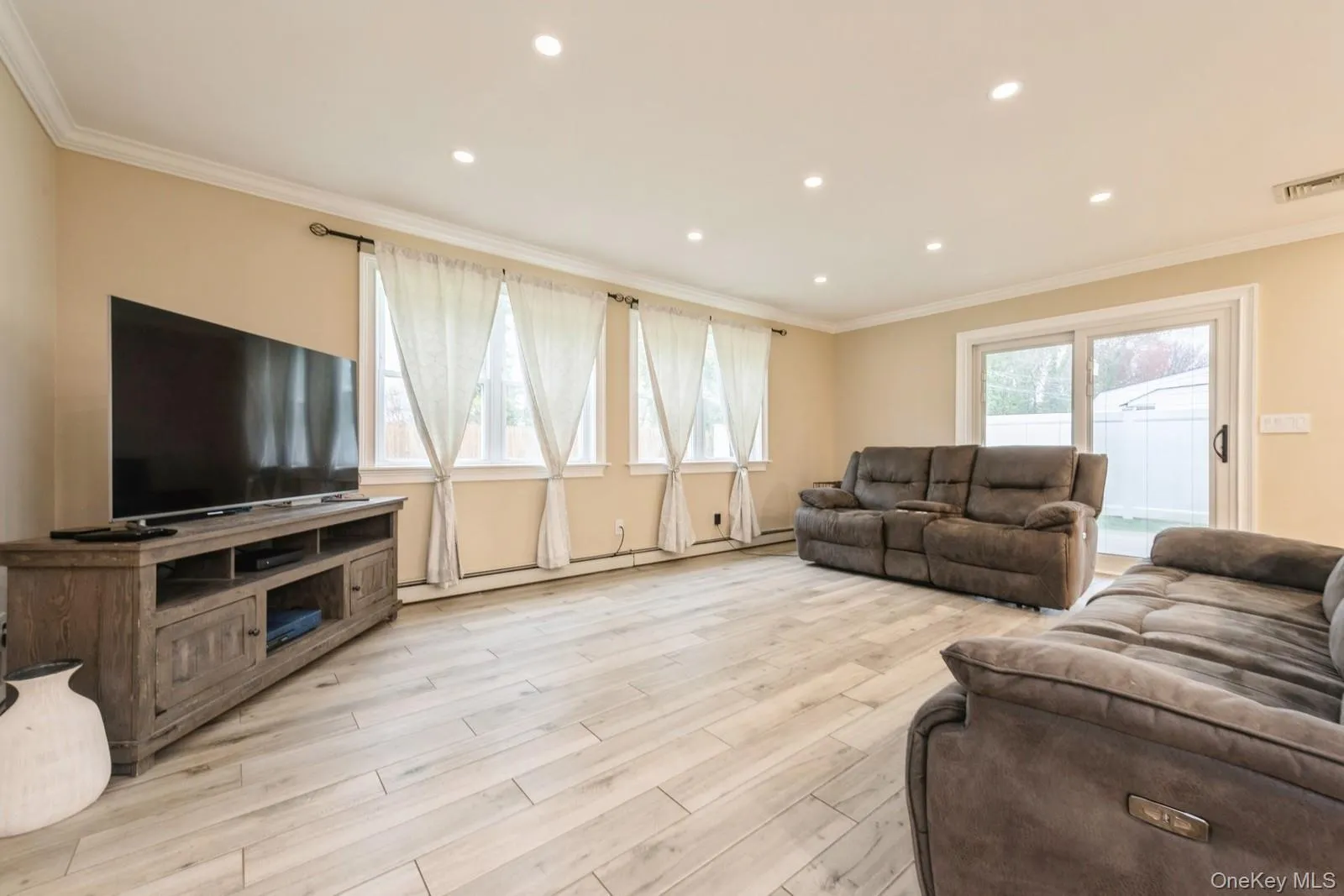 Living area with crown molding, a baseboard heating unit, recessed lighting, plenty of natural light, and light wood-style floors Living area with crown molding, a baseboard heating unit, recessed lighting, plenty of natural light, and light wood-style floors
