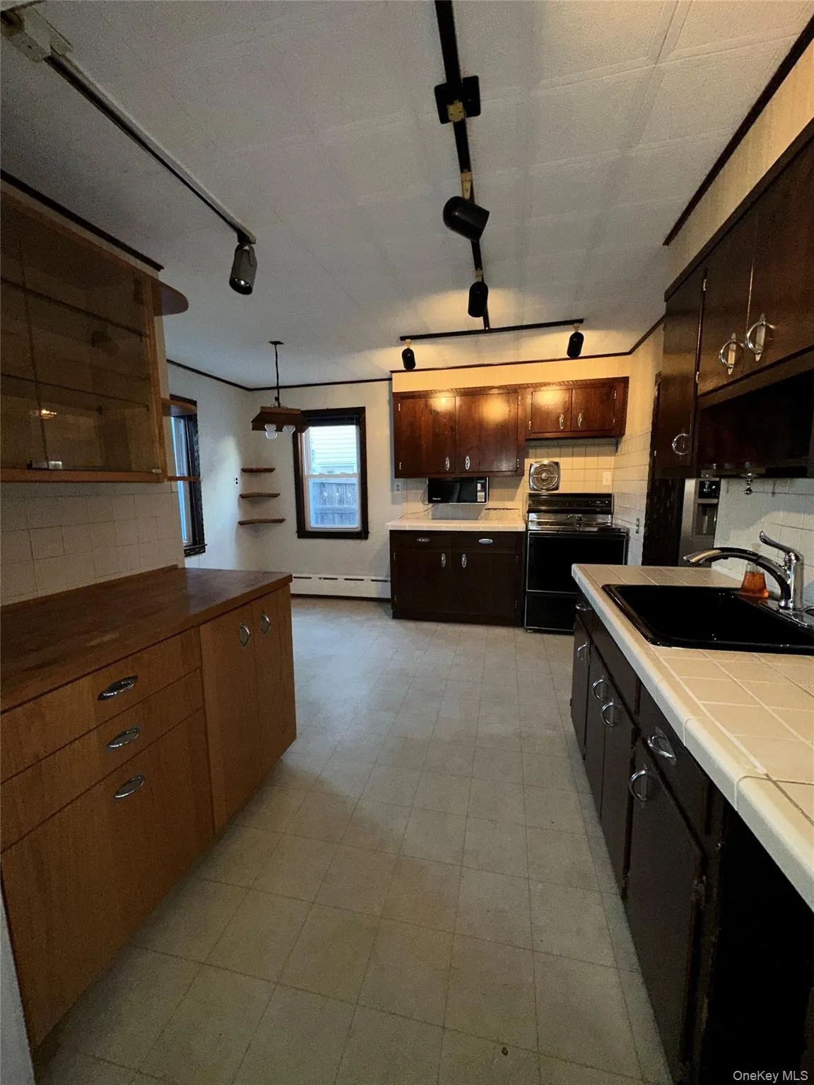 Kitchen featuring backsplash, rail lighting, tile countertops, and black appliances Kitchen featuring backsplash, rail lighting, tile countertops, and black appliances