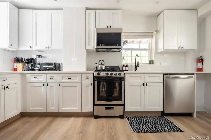 Kitchen featuring appliances with stainless steel finishes, white cabinets, tasteful backsplash, and light wood-style flooring Kitchen featuring appliances with stainless steel finishes, white cabinets, tasteful backsplash, and light wood-style flooring