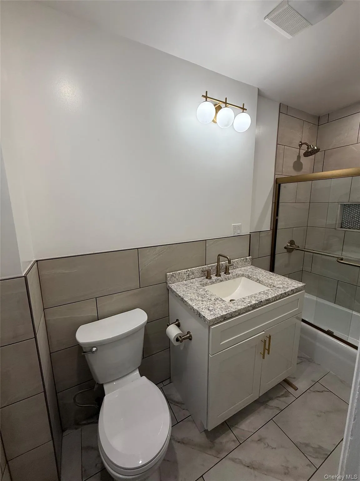 Bathroom with tile walls, wainscoting, enclosed tub / shower combo, vanity, and light marble finish floors Bathroom with tile walls, wainscoting, enclosed tub / shower combo, vanity, and light marble finish floors