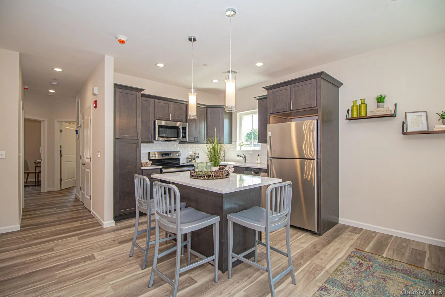 Kitchen featuring dark brown cabinets, a breakfast bar area, appliances with stainless steel finishes, a kitchen island, and hanging light fixtures Kitchen featuring dark brown cabinets, a breakfast bar area, appliances with stainless steel finishes, a kitchen island, and hanging light fixtures