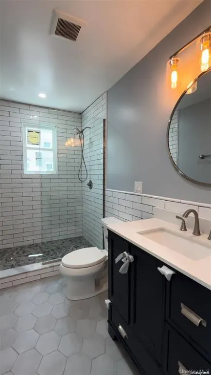 Full bathroom featuring vanity, a shower stall, tile walls, light tile patterned floors, and a wainscoted wall Full bathroom featuring vanity, a shower stall, tile walls, light tile patterned floors, and a wainscoted wall
