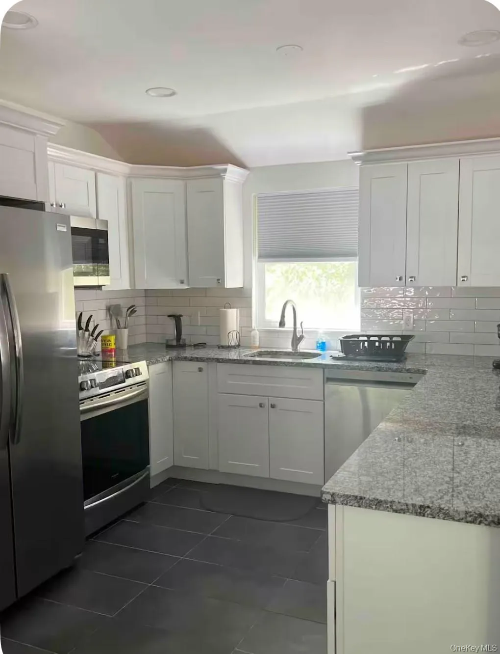 Kitchen featuring stainless steel appliances, tasteful backsplash, white cabinets, dark tile patterned floors, and light stone countertops Kitchen featuring stainless steel appliances, tasteful backsplash, white cabinets, dark tile patterned floors, and light stone countertops