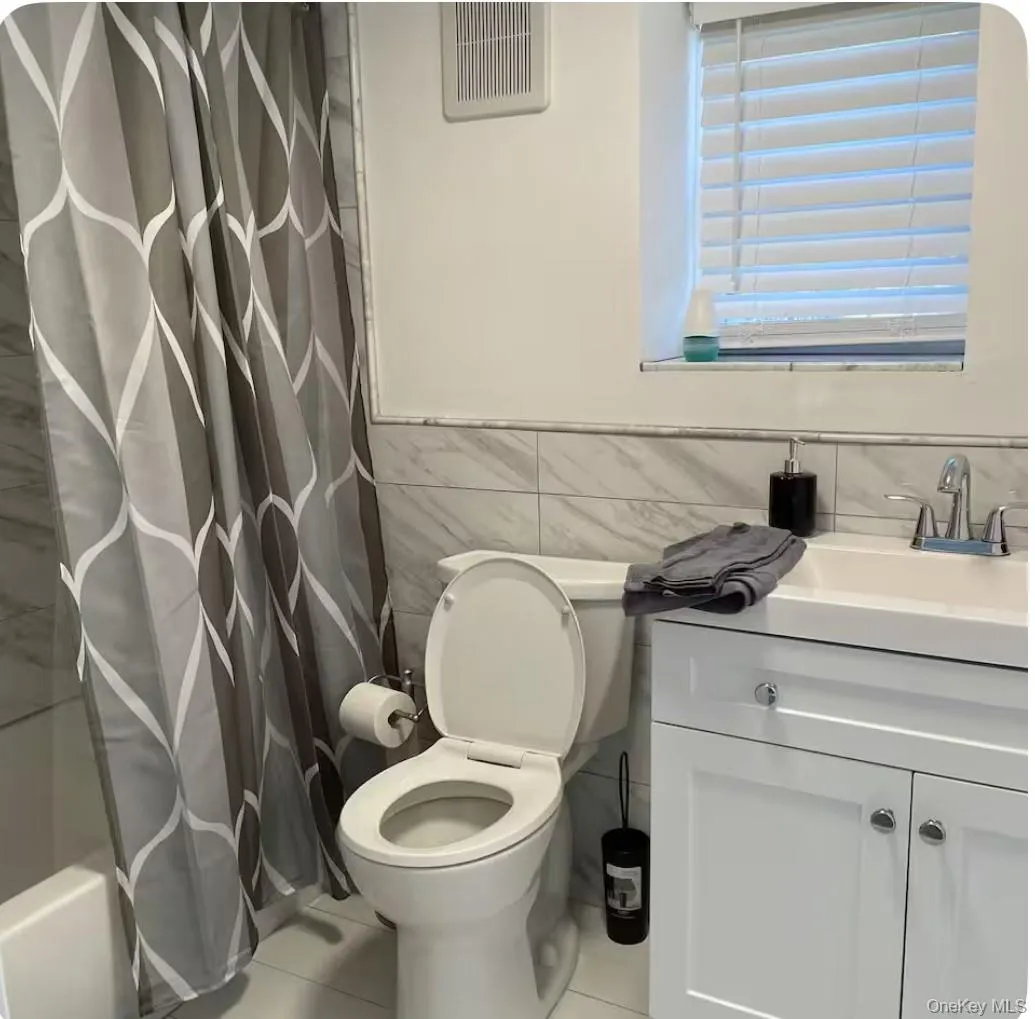 Bathroom featuring tile walls, shower / bath combo with shower curtain, vanity, and tile patterned floors Bathroom featuring tile walls, shower / bath combo with shower curtain, vanity, and tile patterned floors
