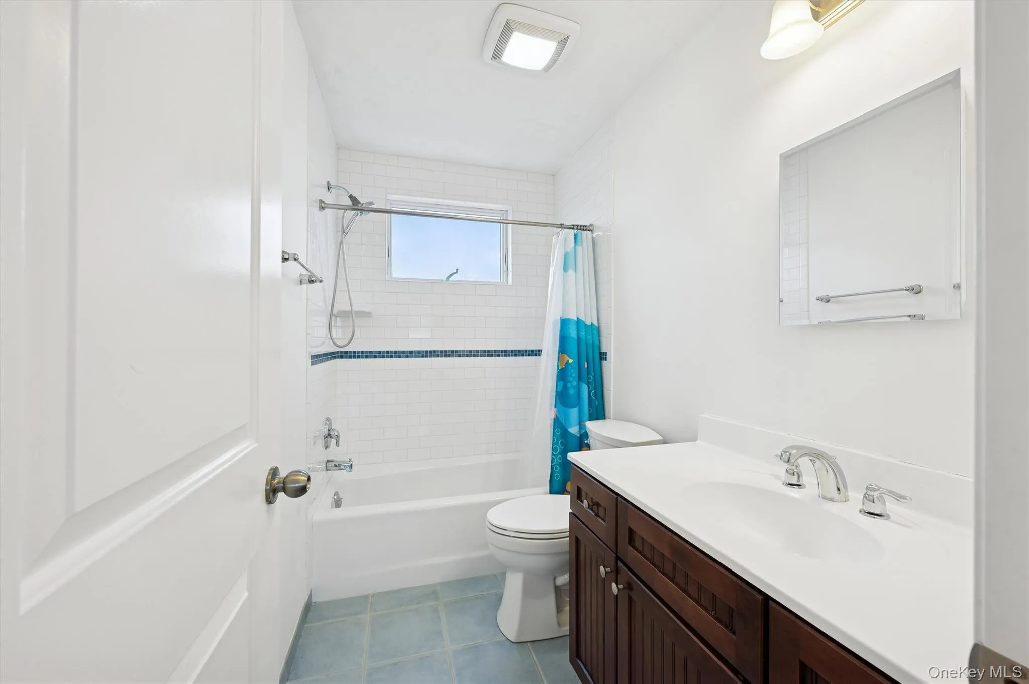 Bathroom featuring shower / tub combo with curtain, vanity, and dark tile patterned flooring Bathroom featuring shower / tub combo with curtain, vanity, and dark tile patterned flooring