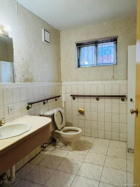 Bathroom with wallpapered walls, wainscoting, and tile walls Bathroom with wallpapered walls, wainscoting, and tile walls