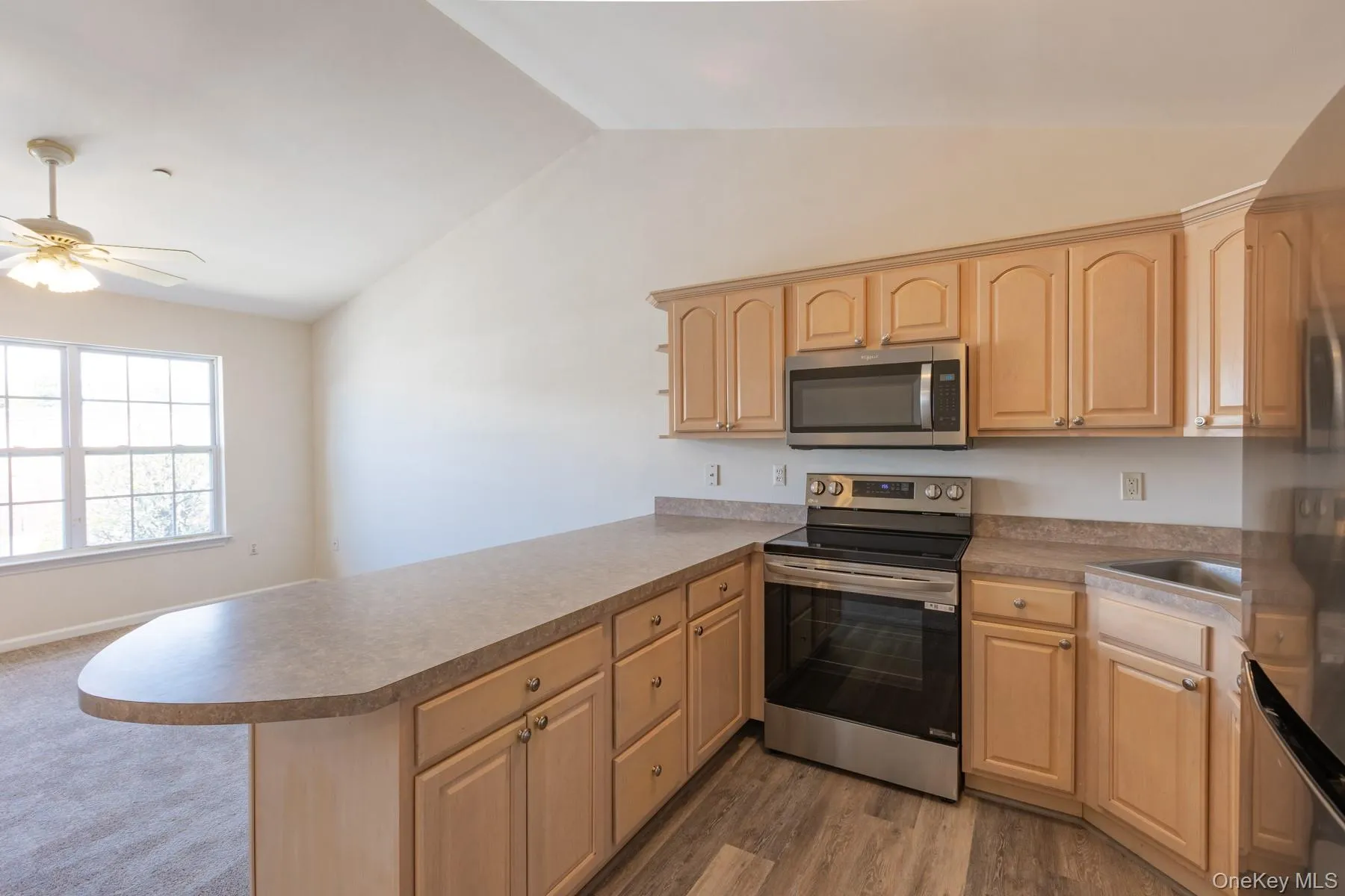Kitchen with stainless steel appliances, light brown cabinetry, vaulted ceiling, a peninsula, and a ceiling fan Kitchen with stainless steel appliances, light brown cabinetry, vaulted ceiling, a peninsula, and a ceiling fan