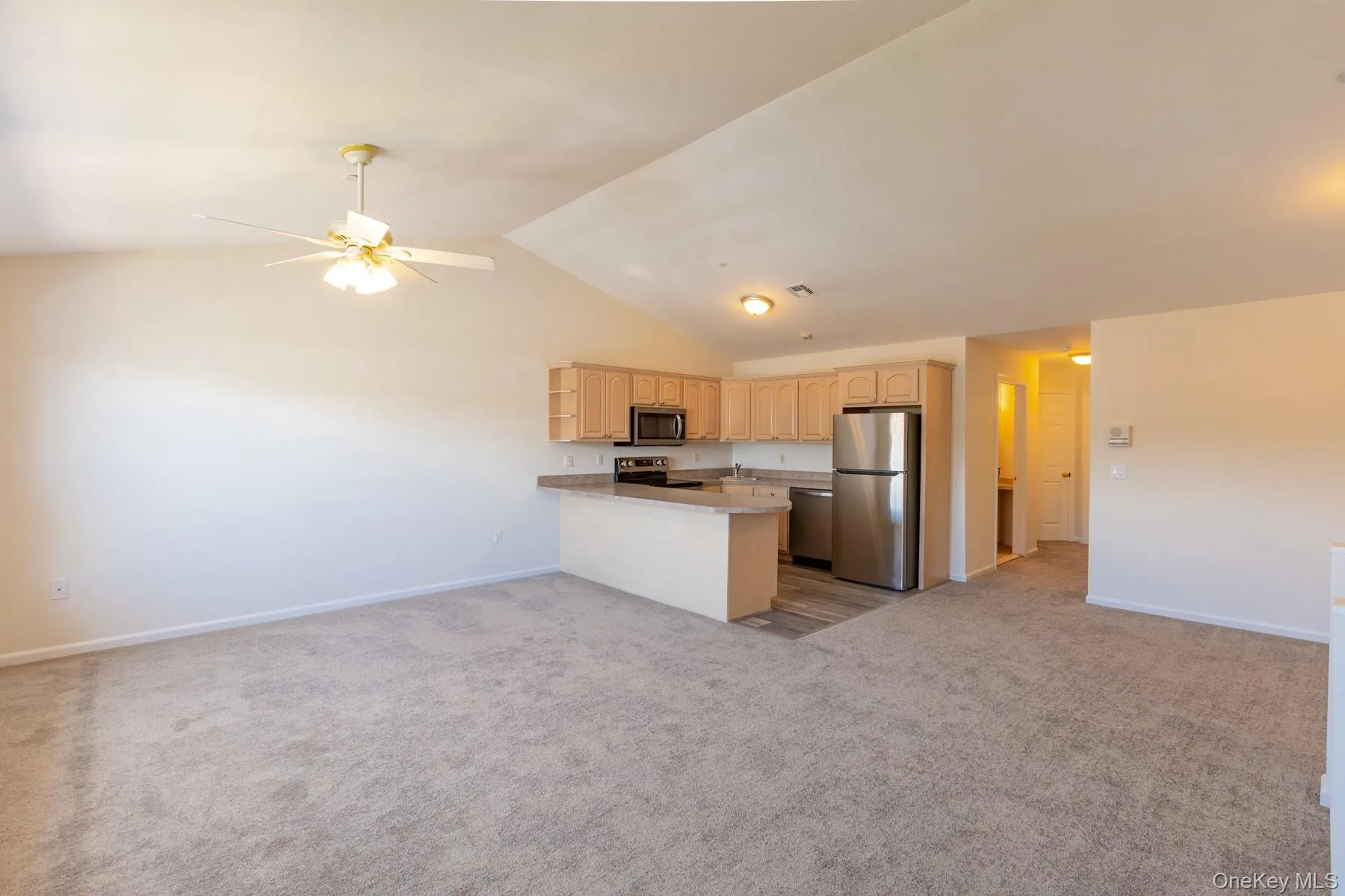 Kitchen featuring open floor plan, stainless steel appliances, light brown cabinets, light countertops, and light colored carpet Kitchen featuring open floor plan, stainless steel appliances, light brown cabinets, light countertops, and light colored carpet
