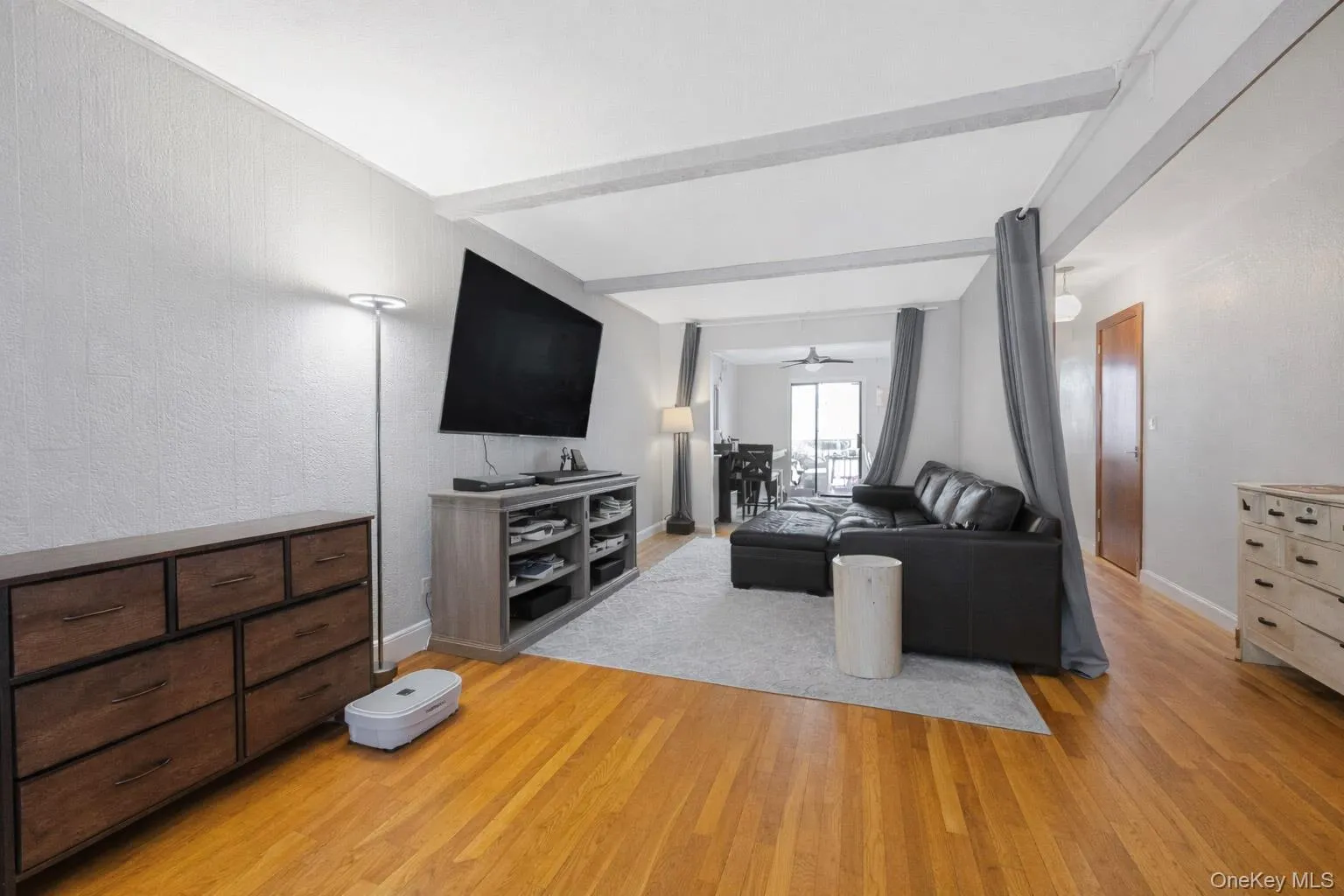 Living room featuring beam ceiling, light wood-type flooring, and a textured wall Living room featuring beam ceiling, light wood-type flooring, and a textured wall