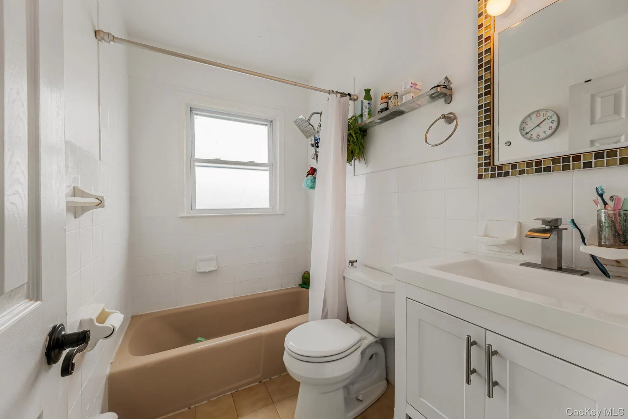 Full bath with vanity, shower / bathtub combination with curtain, tile walls, light tile patterned floors, and backsplash Full bath with vanity, shower / bathtub combination with curtain, tile walls, light tile patterned floors, and backsplash