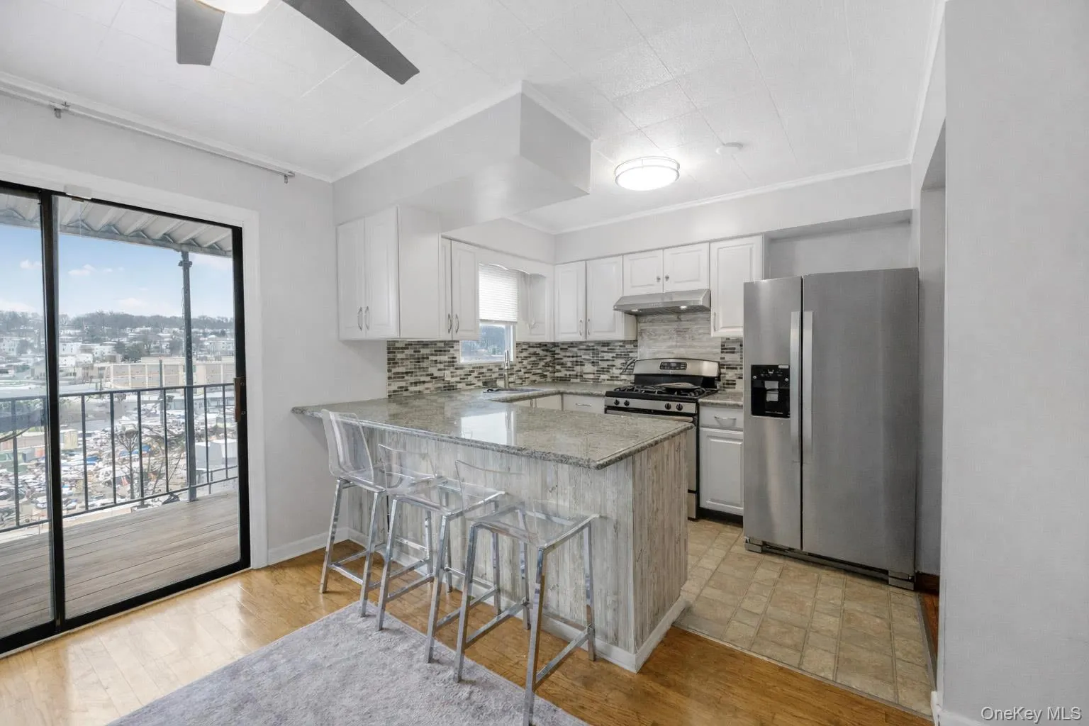 Kitchen featuring stainless steel appliances, white cabinets, light stone countertops, a kitchen breakfast bar, and crown molding Kitchen featuring stainless steel appliances, white cabinets, light stone countertops, a kitchen breakfast bar, and crown molding