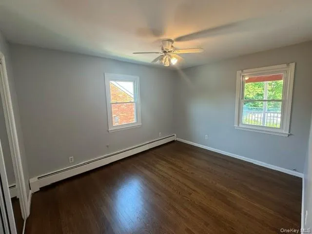 Empty room with ceiling fan, a wealth of natural light, dark hardwood / wood-style flooring, and a baseboard radiator Empty room with ceiling fan, a wealth of natural light, dark hardwood / wood-style flooring, and a baseboard radiator