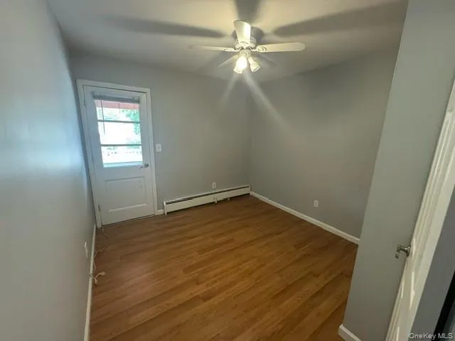 Unfurnished room with ceiling fan, a baseboard heating unit, and hardwood / wood-style flooring Unfurnished room with ceiling fan, a baseboard heating unit, and hardwood / wood-style flooring