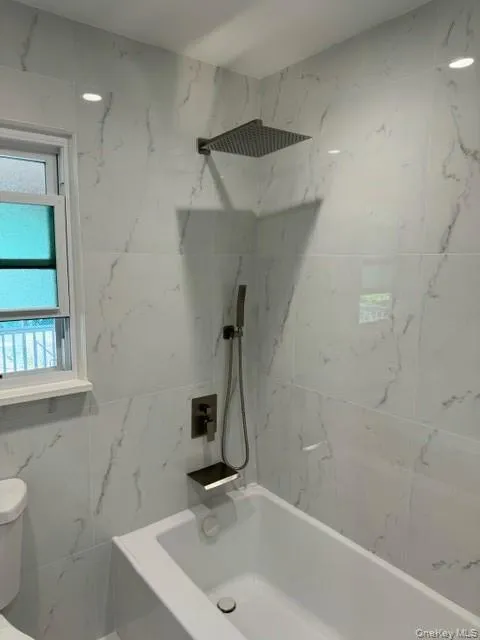 Bathroom with tiled shower / bath combo, toilet, and tile walls Bathroom with tiled shower / bath combo, toilet, and tile walls
