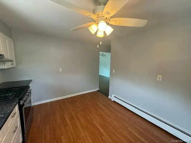 Kitchen with dark hardwood / wood-style floors, white cabinets, a baseboard heating unit, ceiling fan, and stainless steel gas stove Kitchen with dark hardwood / wood-style floors, white cabinets, a baseboard heating unit, ceiling fan, and stainless steel gas stove