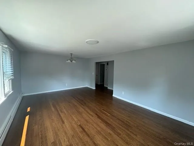 Empty room with baseboard heating, dark hardwood / wood-style floors, and an inviting chandelier Empty room with baseboard heating, dark hardwood / wood-style floors, and an inviting chandelier