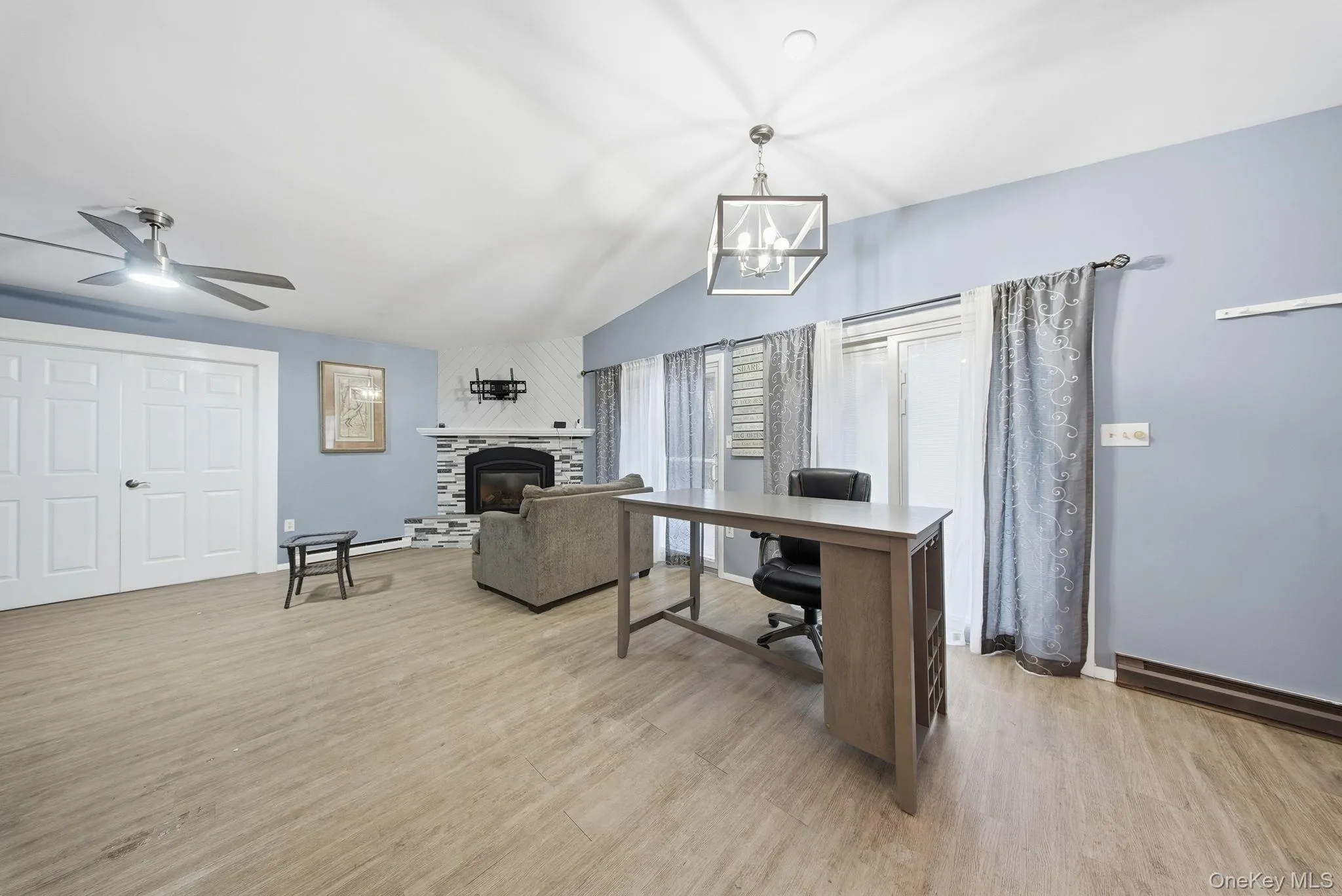 Office space with a glass covered fireplace, lofted ceiling, light wood-style floors, and a ceiling fan Office space with a glass covered fireplace, lofted ceiling, light wood-style floors, and a ceiling fan