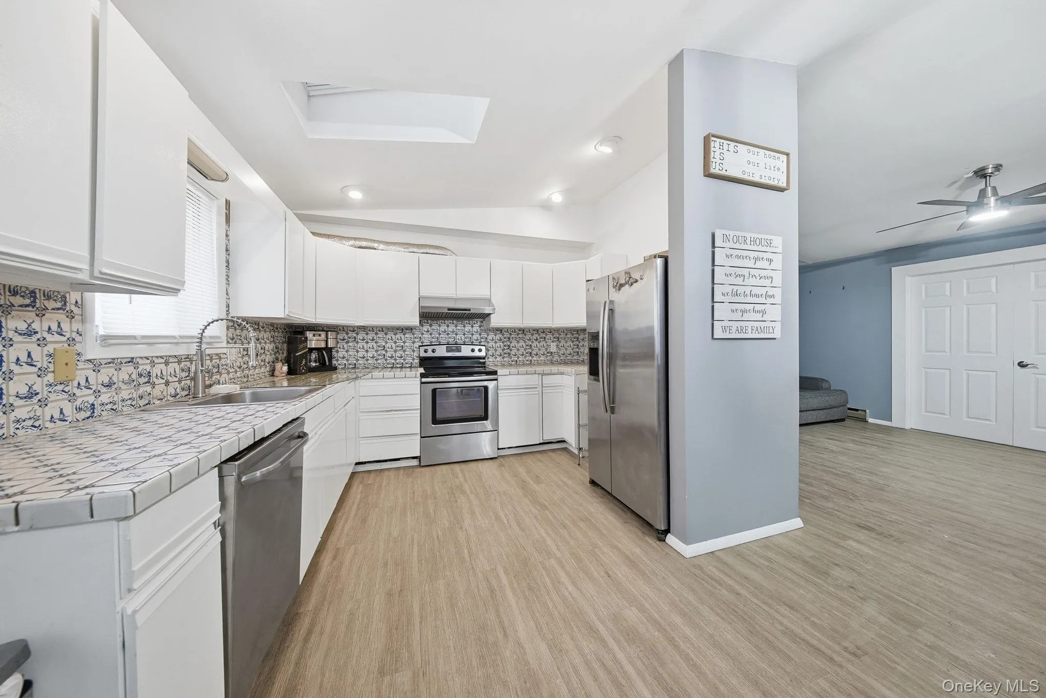 Kitchen featuring tile countertops, white cabinetry, vaulted ceiling, appliances with stainless steel finishes, and light wood-style flooring Kitchen featuring tile countertops, white cabinetry, vaulted ceiling, appliances with stainless steel finishes, and light wood-style flooring
