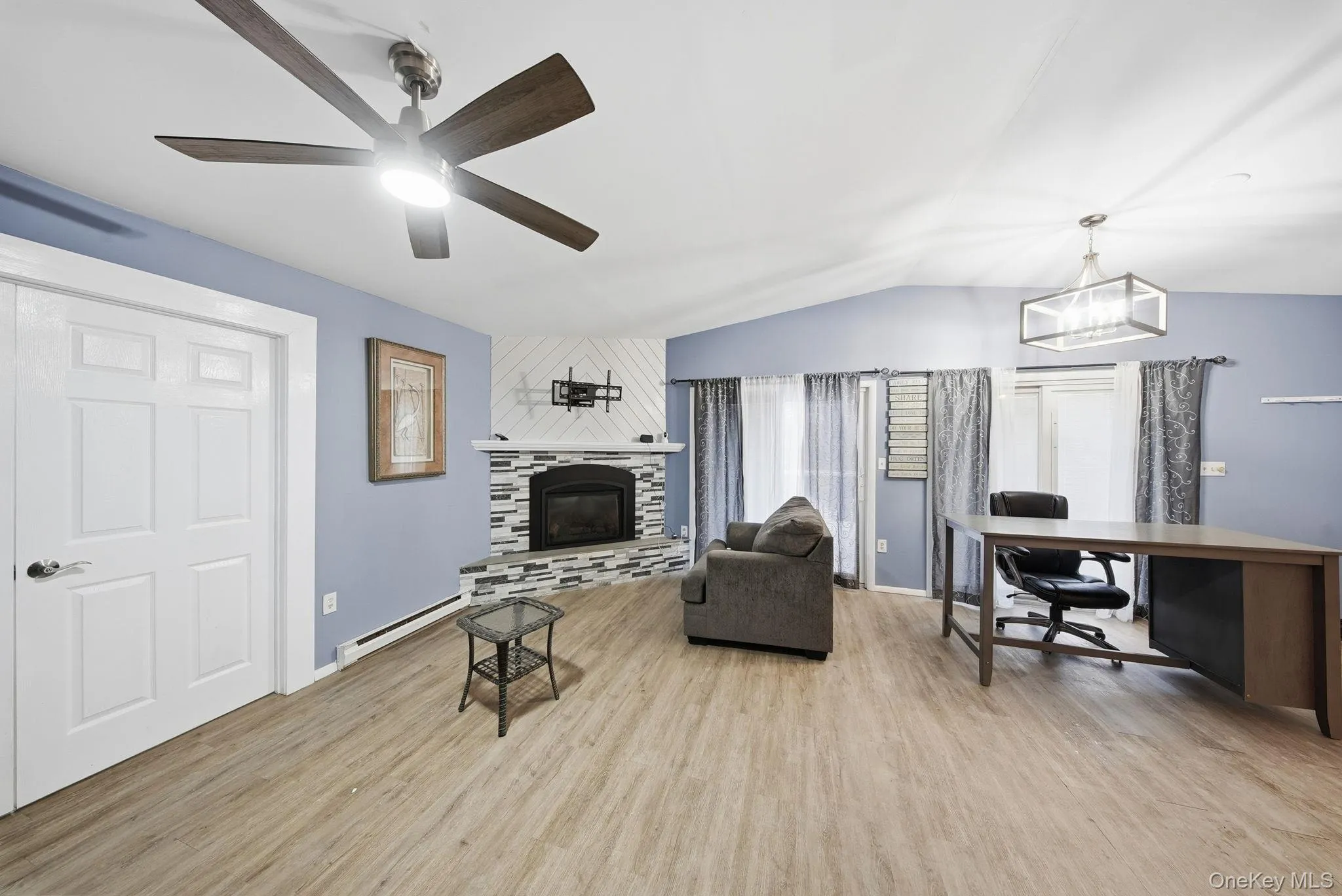 Living room featuring an office area, a baseboard radiator, a tiled fireplace, light wood-type flooring, and vaulted ceiling Living room featuring an office area, a baseboard radiator, a tiled fireplace, light wood-type flooring, and vaulted ceiling