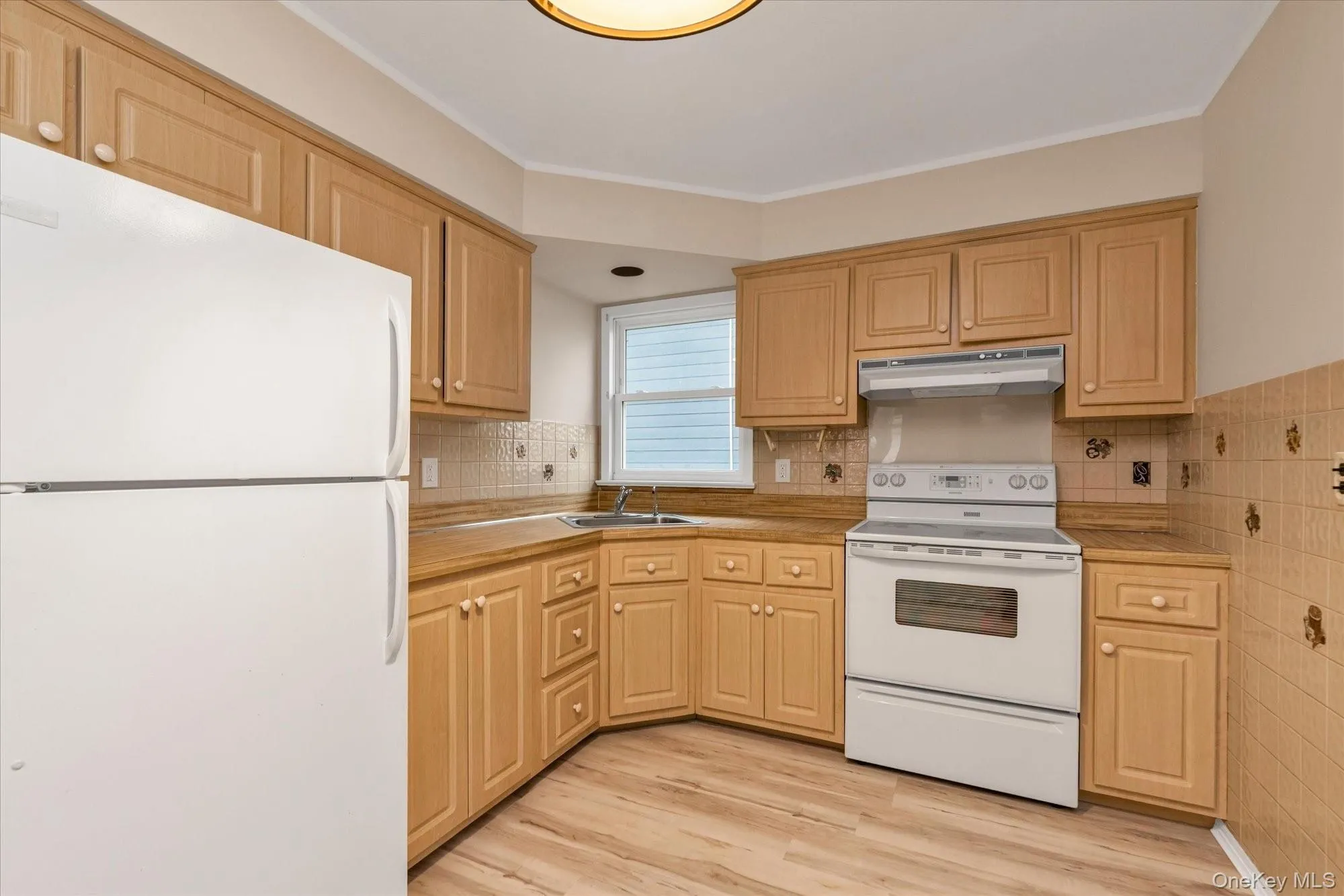 Kitchen with white appliances, light countertops, under cabinet range hood, light wood-type flooring, and light brown cabinetry Kitchen with white appliances, light countertops, under cabinet range hood, light wood-type flooring, and light brown cabinetry